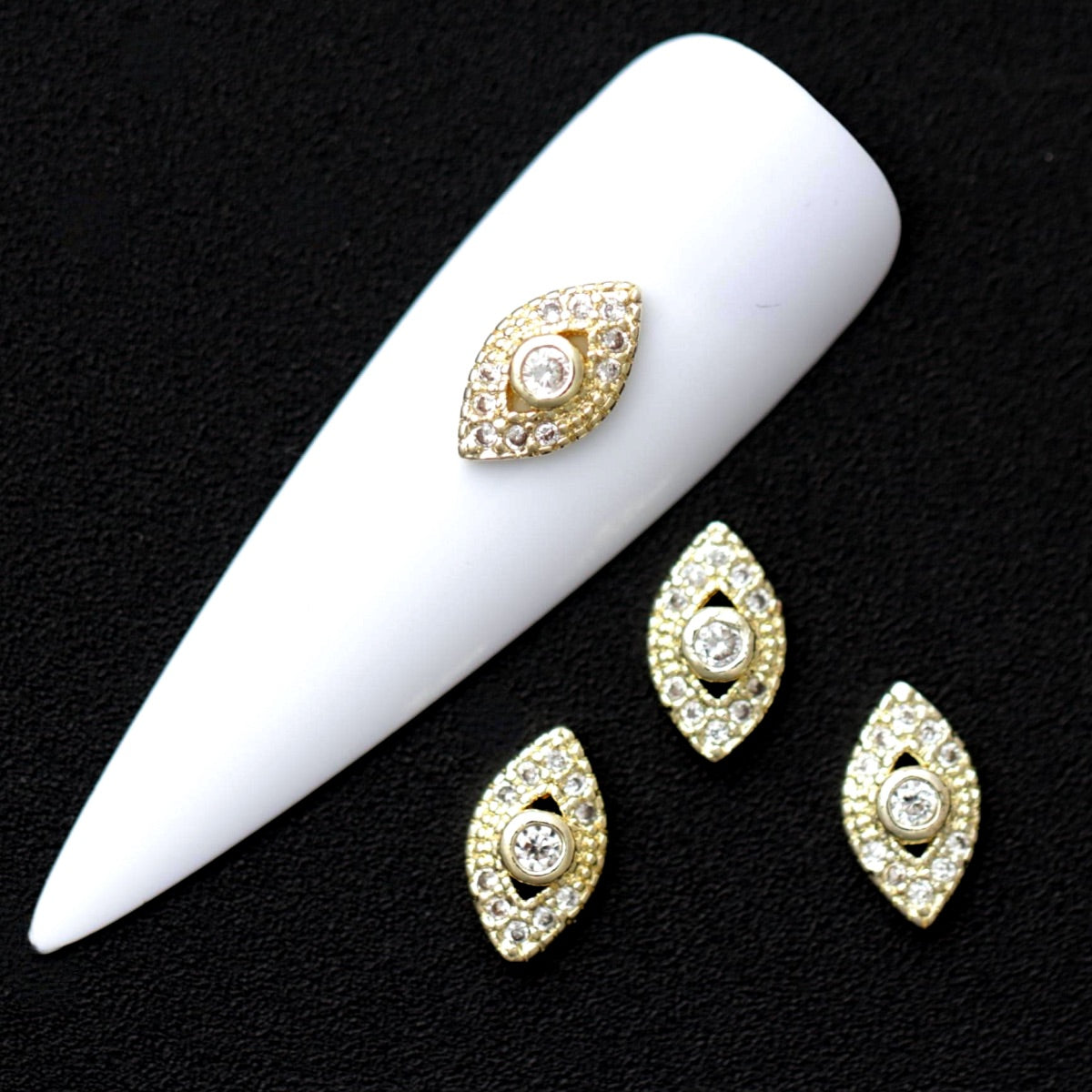 Gold 10×6 mm marquise-shaped nail charms with crystal CZ centre and halo of tiny clear stones displayed on a white nail tip against a black background