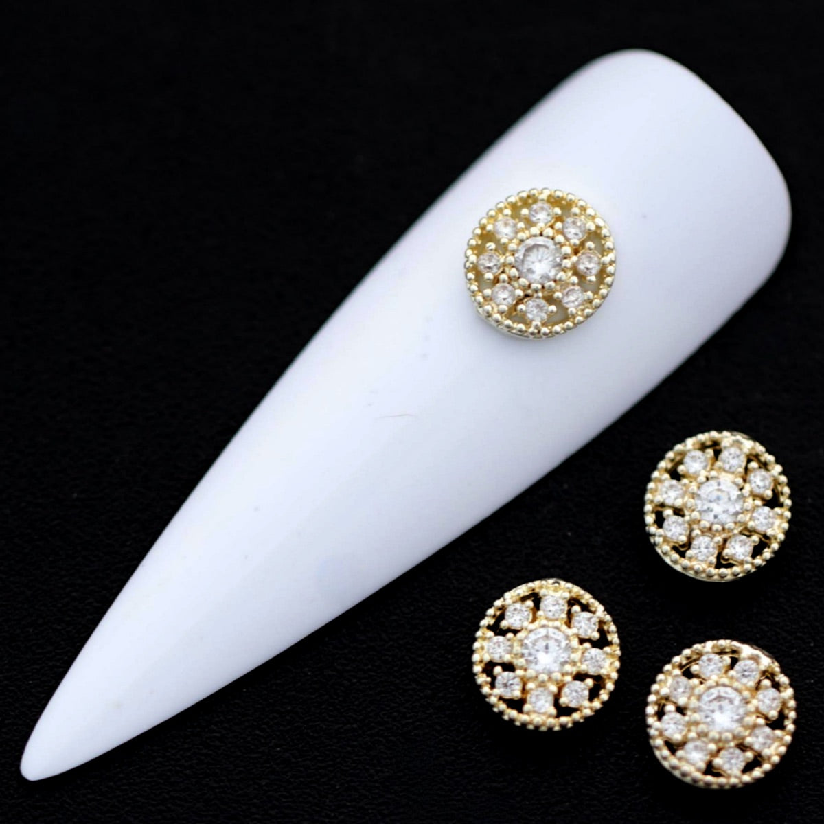 Gold 7 mm round medallion nail charms with central crystal CZ and surrounding mini stones displayed on a white nail tip against a black background