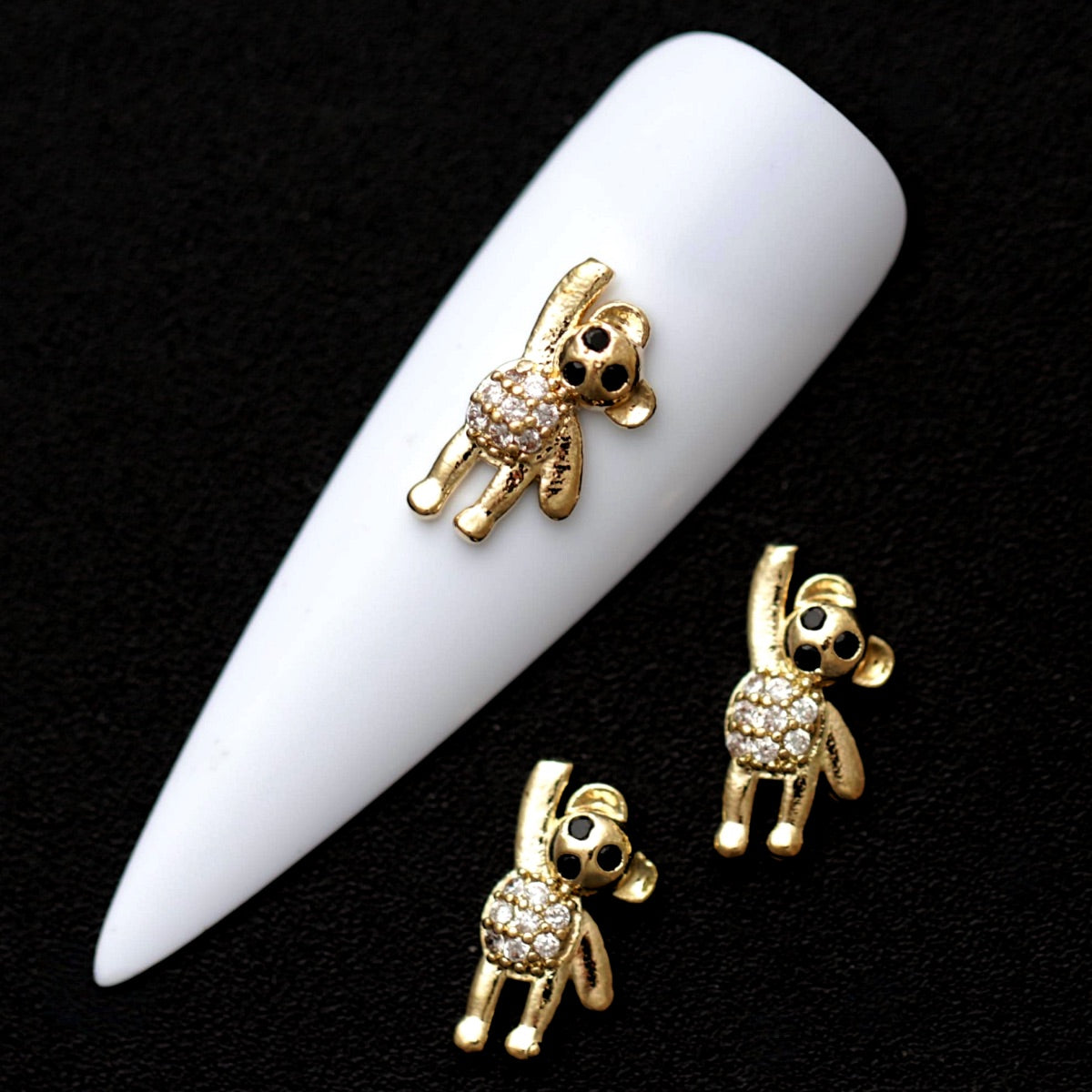 Gold 12×7 mm waving teddy bear nail charms with crystal CZ stones displayed on a white nail tip against a black background