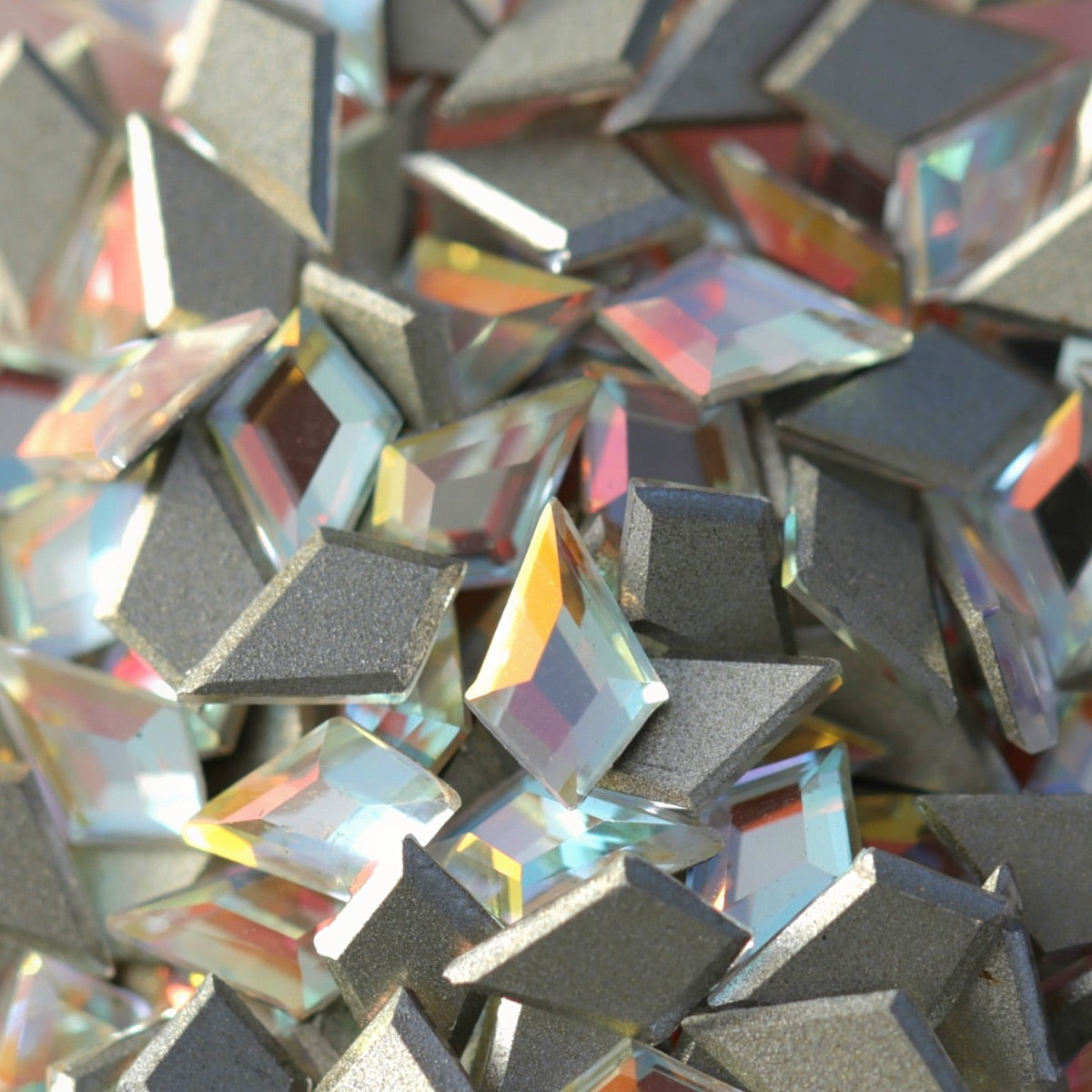 Pile of faceted K9 crystal deltoid flatbacks Crystal Gold Shimmer showing rainbow refractions gold shimmer and silver foil base on light pink surface
