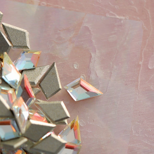 Scattered K9 crystal flatback deltoid rhinestones in Crystal Gold Shimmer with iridescent gold-blue sparkle on pearlescent pink background for nail art
