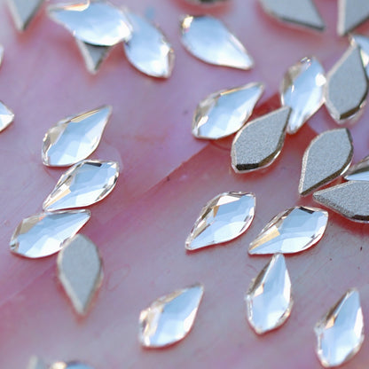 Closeup of clear faceted K9 crystal flatback flame shaped rhinestones showing light refraction and silver metallic base on pink surface