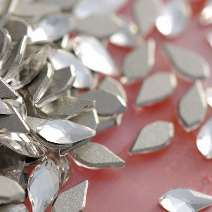 Pile of transparent K9 crystal flatback flame crystals with precision facets and silver backing on soft pink background for luxury nail decoration