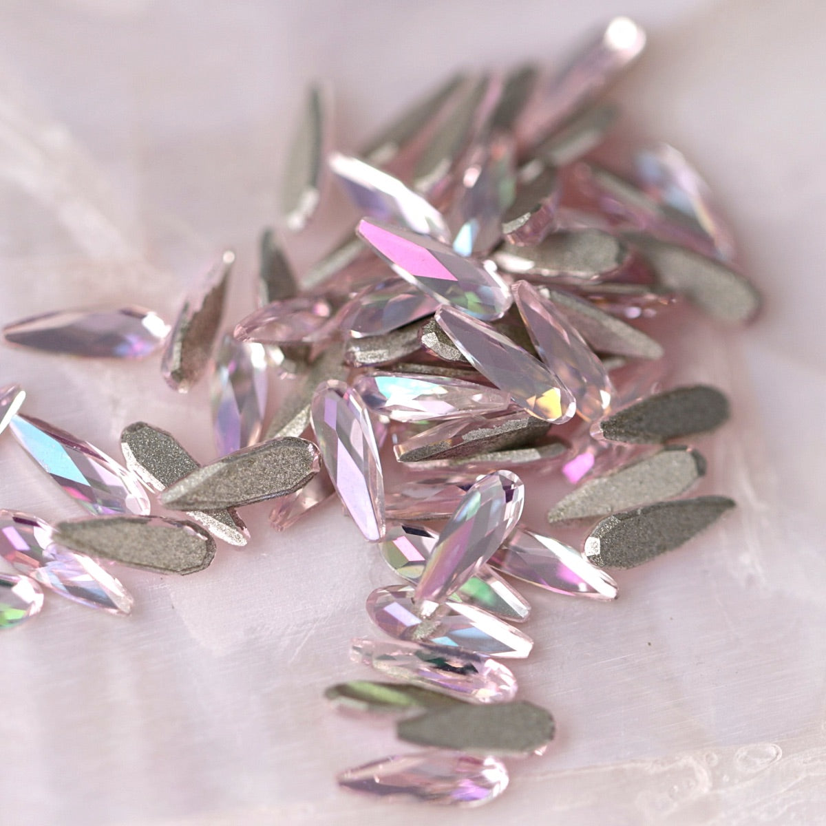 K9 Crystal Flatback Raindrop Luminous Light Rose stones scattered on a light background, showing soft pink teardrop crystals with shimmering facets for nail art and decorations.