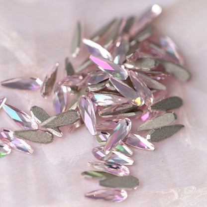 K9 Crystal Flatback Raindrop Luminous Light Rose stones scattered on a light background, showing soft pink teardrop crystals with shimmering facets for nail art and decorations.