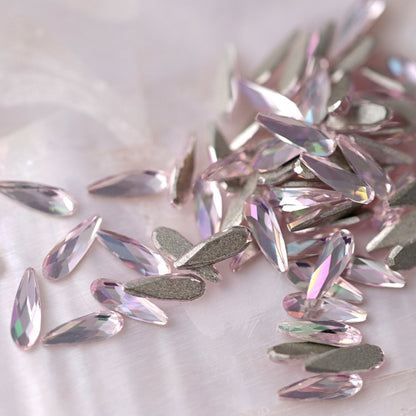 Small group of K9 Crystal Flatback Raindrop Luminous Light Rose stones arranged on a pale surface, showing teardrop-shaped light rose crystals ready for nail art and creative embellishments.