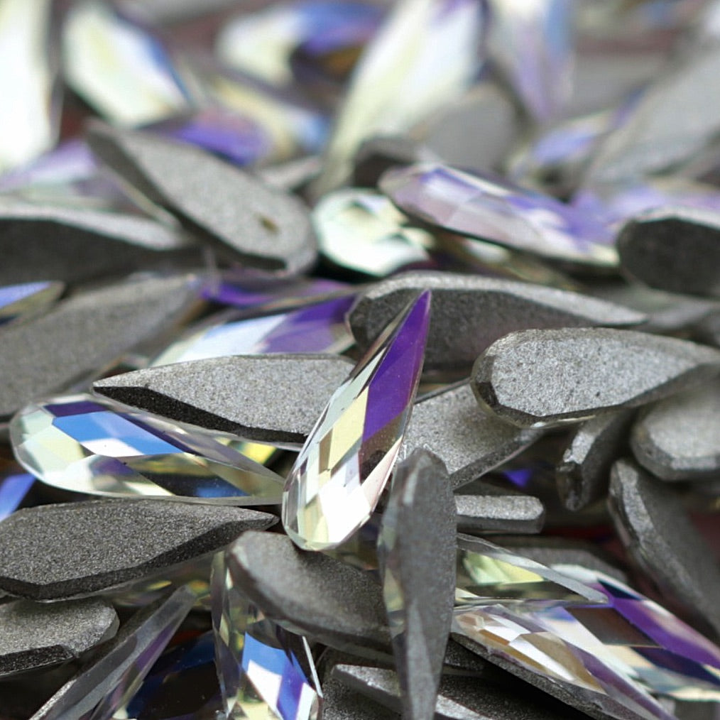 Close-up pile of K9 Crystal flatback raindrop stones in Moonlight color showing translucent facets with lilac and icy blue reflections