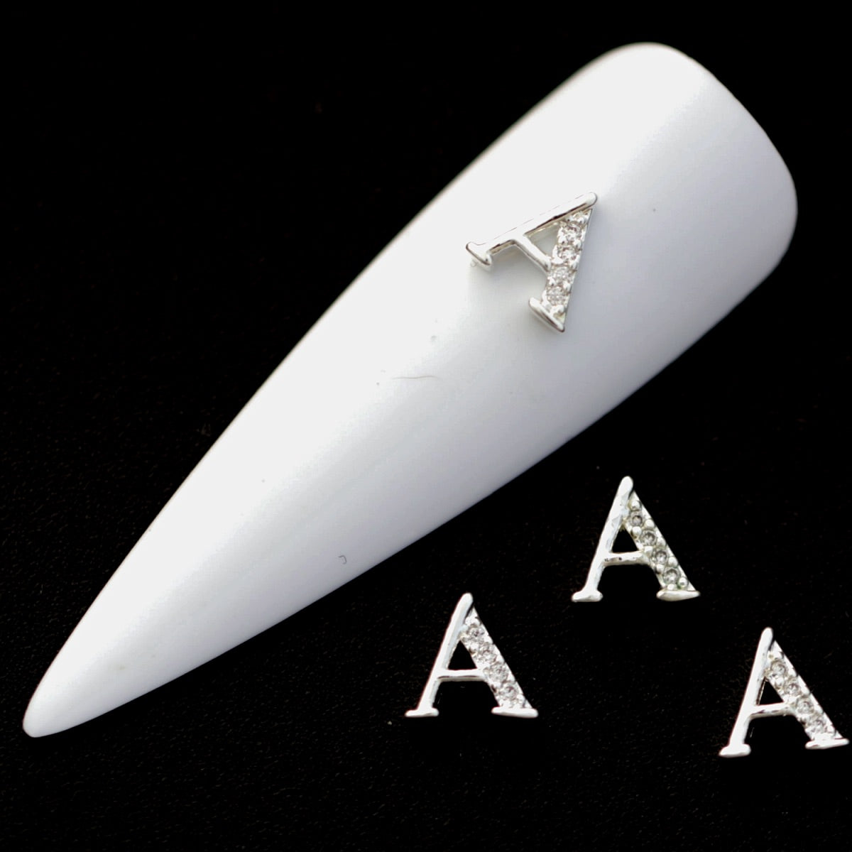 Silver A letter nail charms with crystal CZ accents on a white nail tip against a black background.