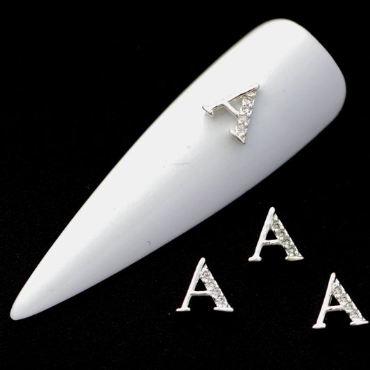 Silver A letter nail charms with crystal CZ accents on a white nail tip against a black background.
