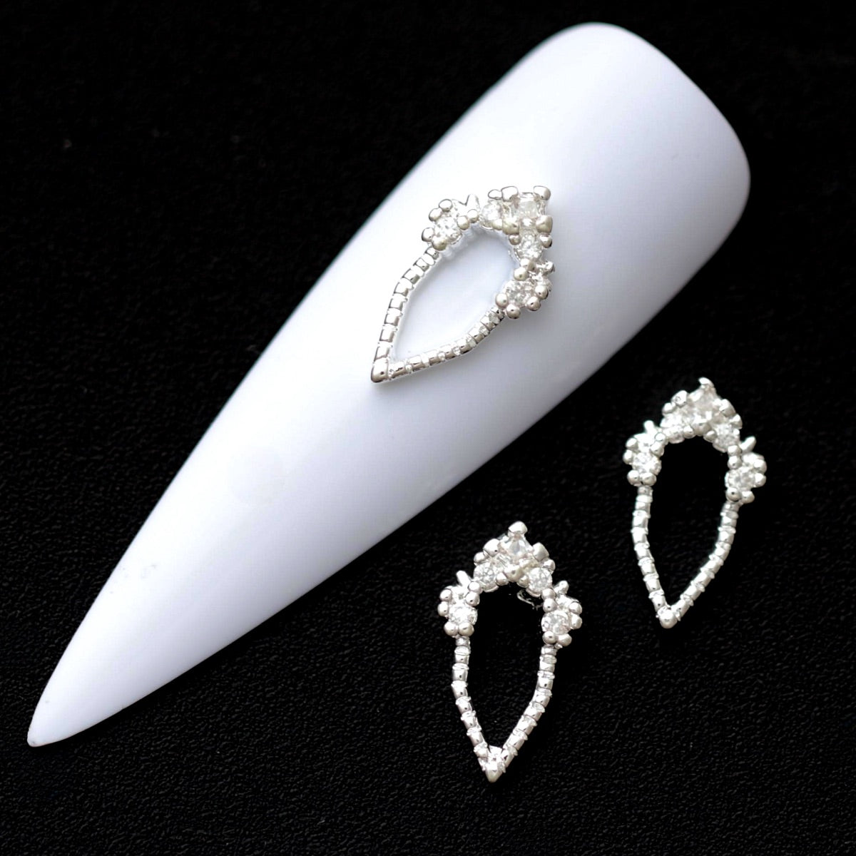 Silver baroque teardrop frame nail charms outlined with crystal cubic zirconia on a white nail tip against a black background