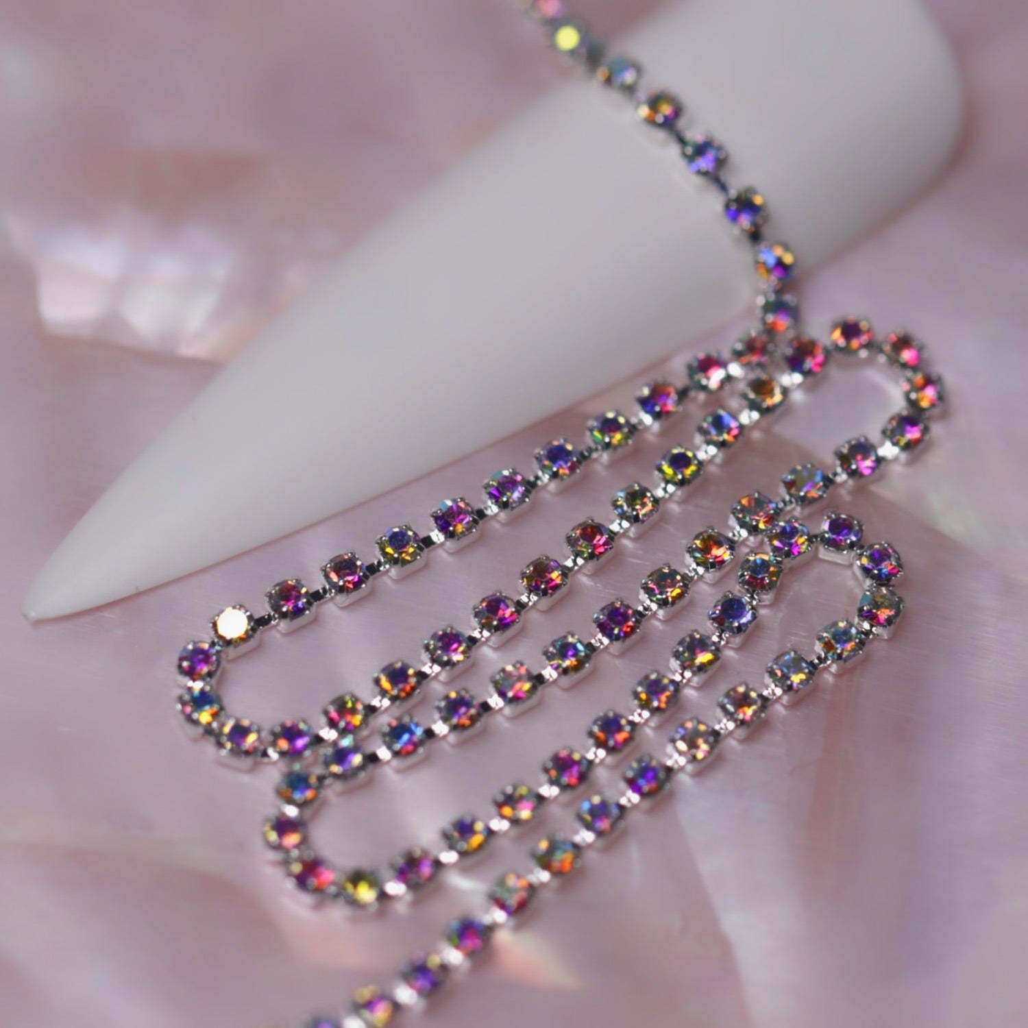 Silver 1.5 mm Crystal AB rhinestone nail art chain laid across a white nail tip