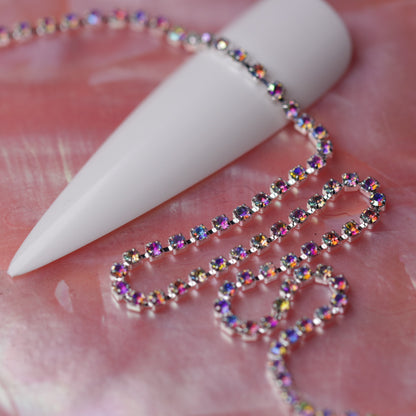 Silver 1.5 mm Crystal AB rhinestone nail art chain laid across a white nail tip