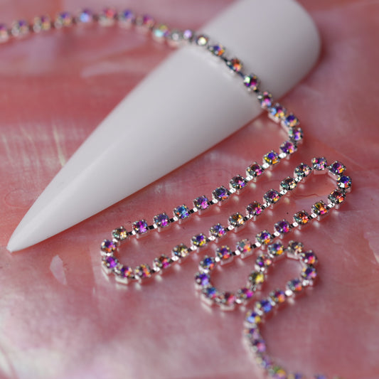 Silver 1.5 mm Crystal AB rhinestone nail art chain laid across a white nail tip