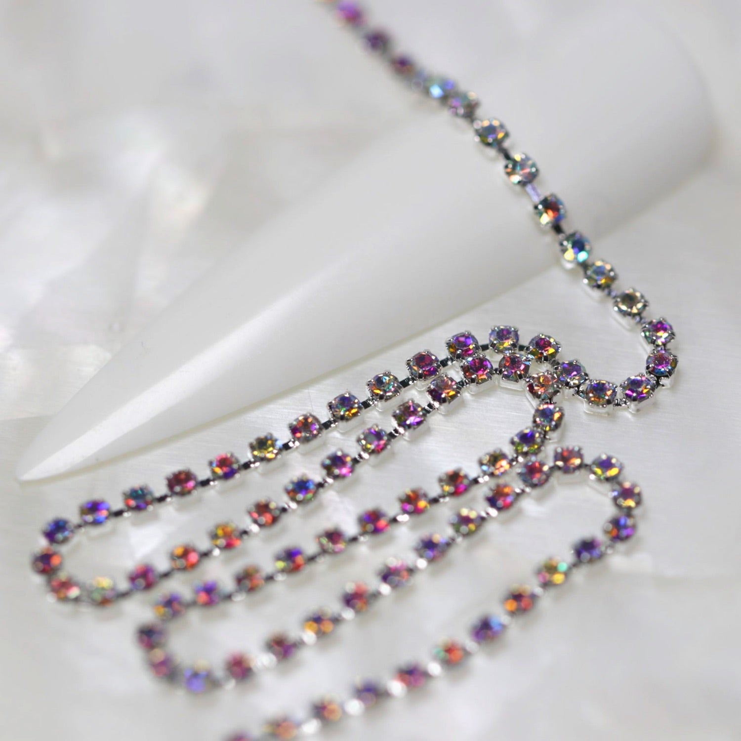 Silver 1.5 mm Crystal AB rhinestone nail art chain laid across a white nail tip