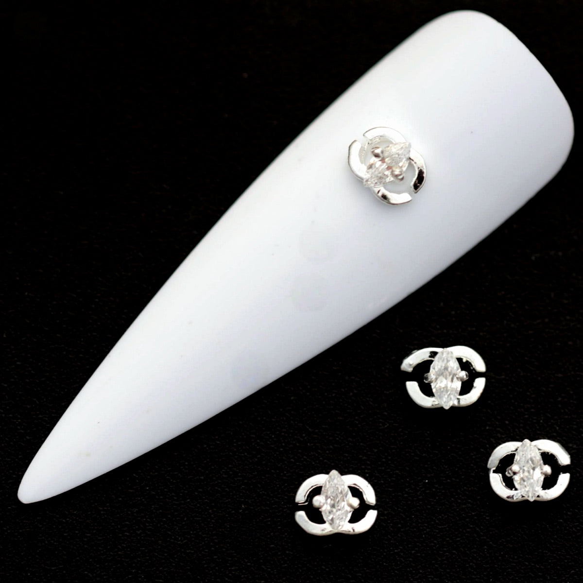 Silver open‑circle nail charms with marquise crystal CZ centres on a white nail tip against a black background.