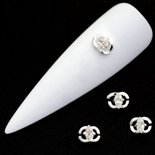 Silver open‑circle nail charms with marquise crystal CZ centres on a white nail tip against a black background.