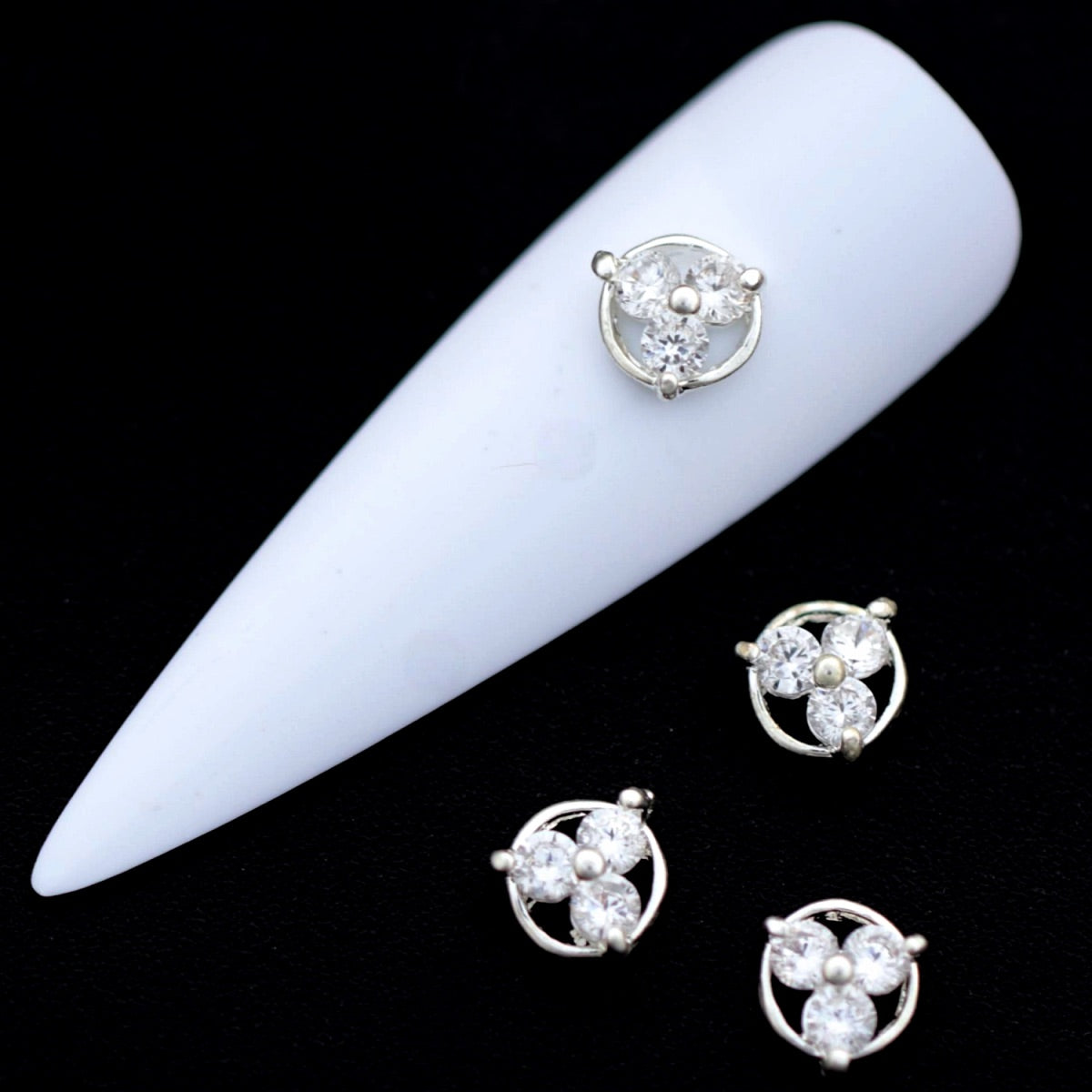 Silver circular nail charms with three crystal‑colored CZ stones on a white nail tip against a black background.