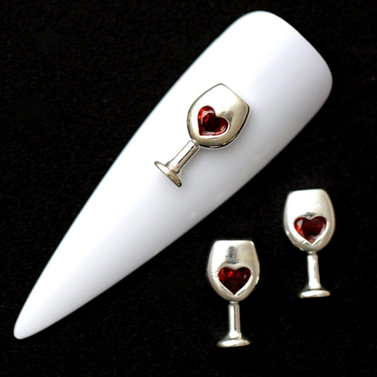 Silver 12×6 mm wine glass nail charms with red heart-shaped CZ stones displayed on a white nail tip against a black background