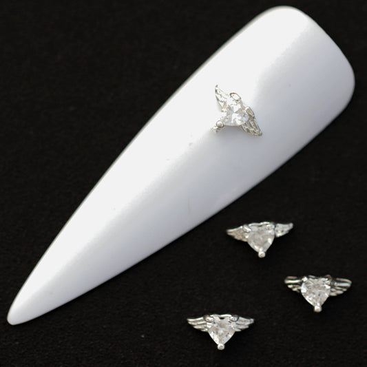 Silver winged heart nail charms with crystal‑colored heart CZ stones on a white nail tip against a black background