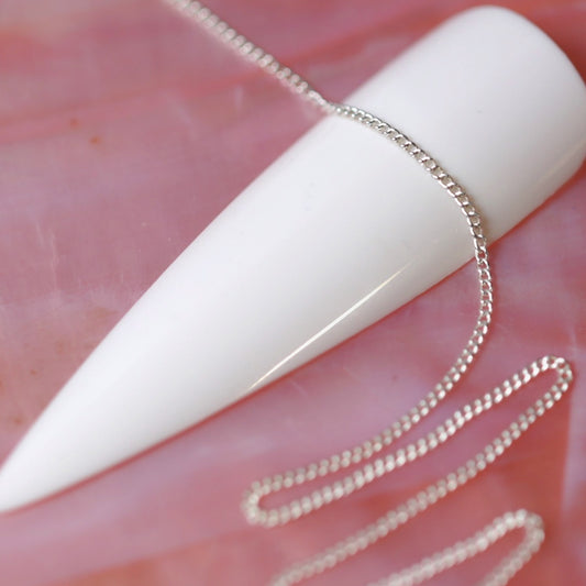 Ultra fine silver chain draped over a long white nail tip on a pink background.