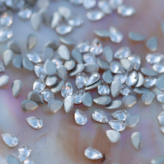 Top view of sparkling clear flatback zircon drop crystals with silver backs, ideal for creating elegant nail art designs and decorations